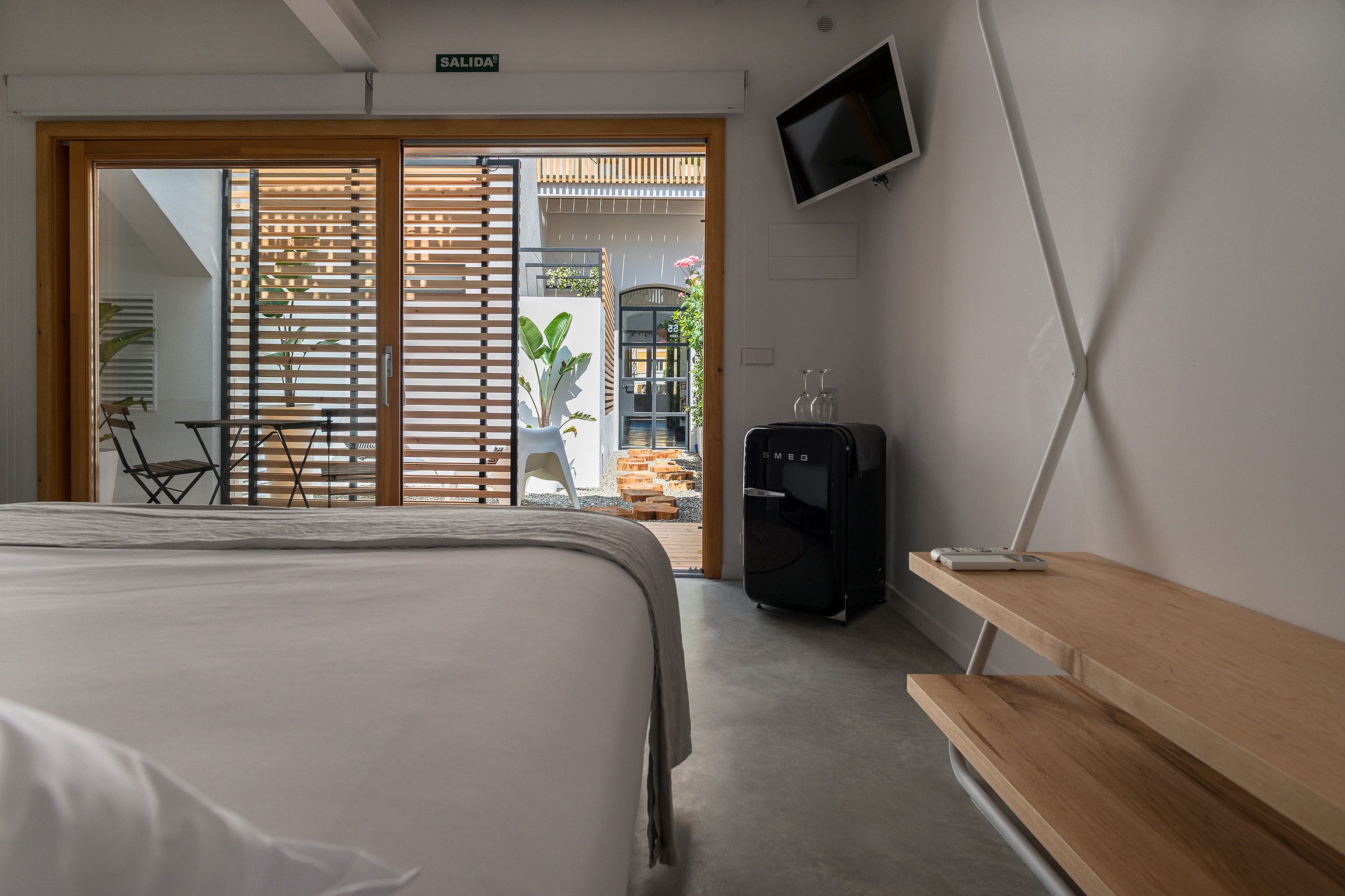 A hotel room with a bed, a desk, a water dispenser, and a TV on the wall.