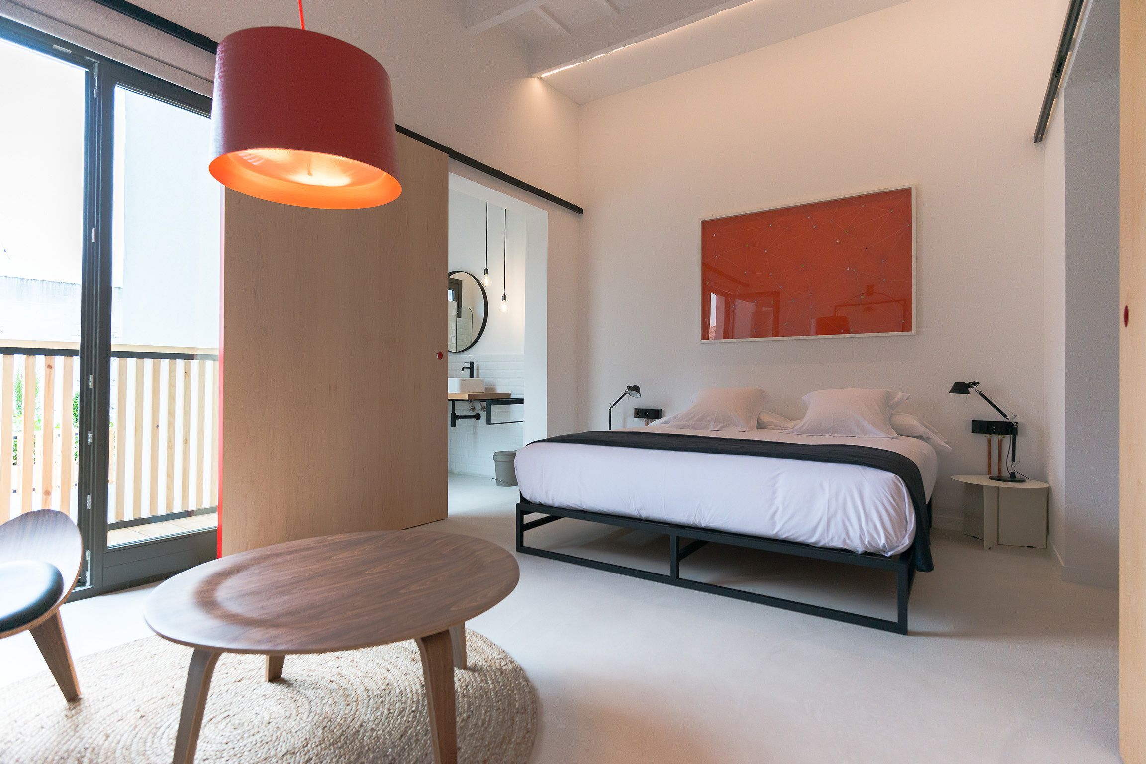 Un dormitorio moderno con una cama, mesitas de noche, una mesa redonda y un ventanal grande.