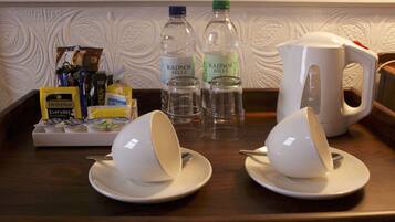 A tray with two white cups, two water bottles, a coffee maker, and a tray of Twinings coffee packets.