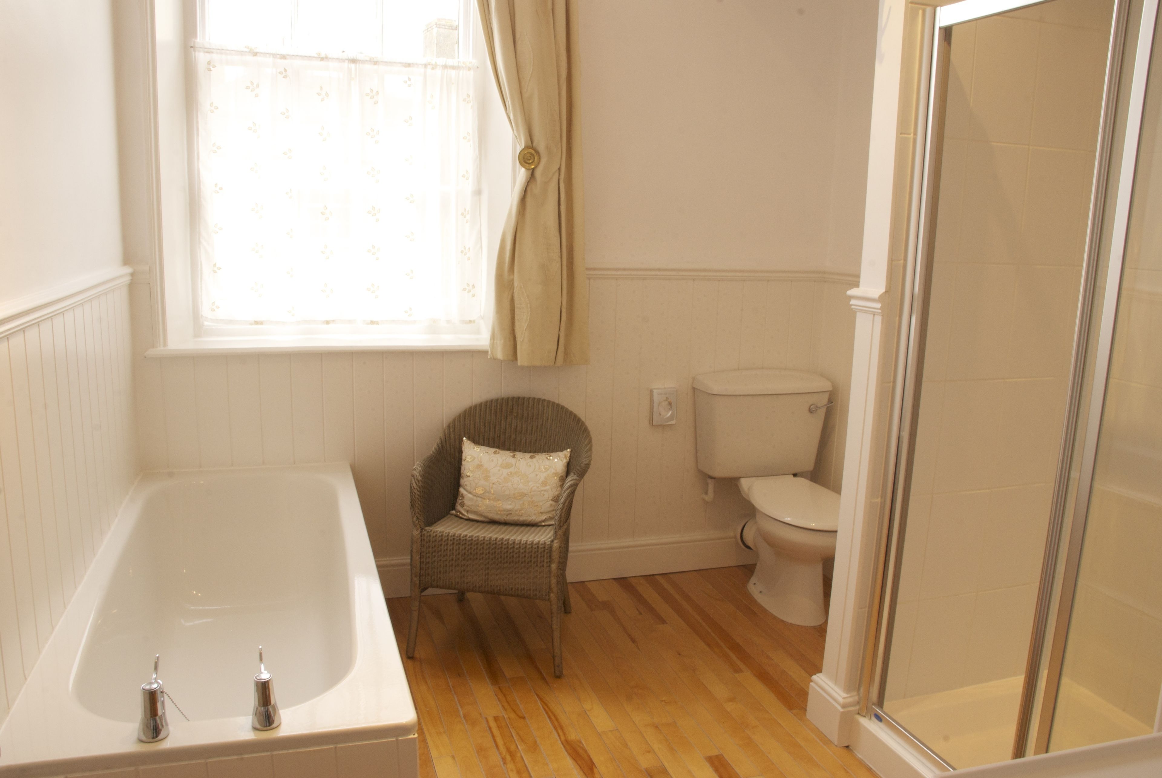 A bathroom with a bathtub, a toilet, a wicker chair, and a shower area.