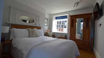 A bedroom with a large bed, a wooden dresser, a mirror, and a television on the wall.