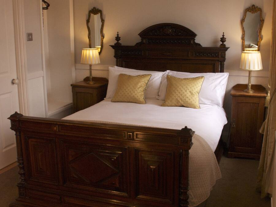 Ein traditionell eingerichtetes Schlafzimmer mit Himmelbett, zwei Nachttischen inklusive Lampen und einem großen Spiegel.