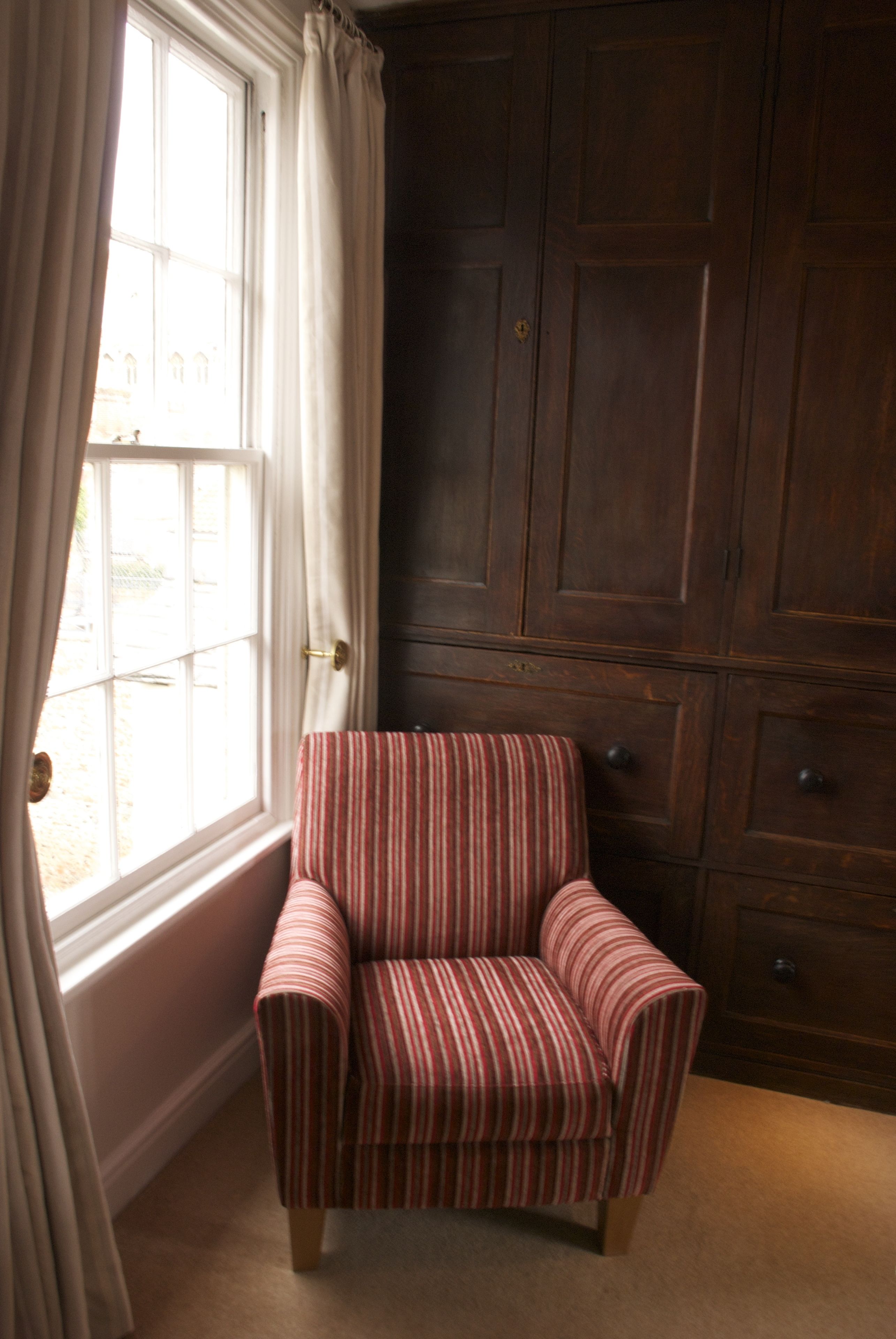 Una habitación con ventana, un sillón a rayas y un mueble de madera oscura.
