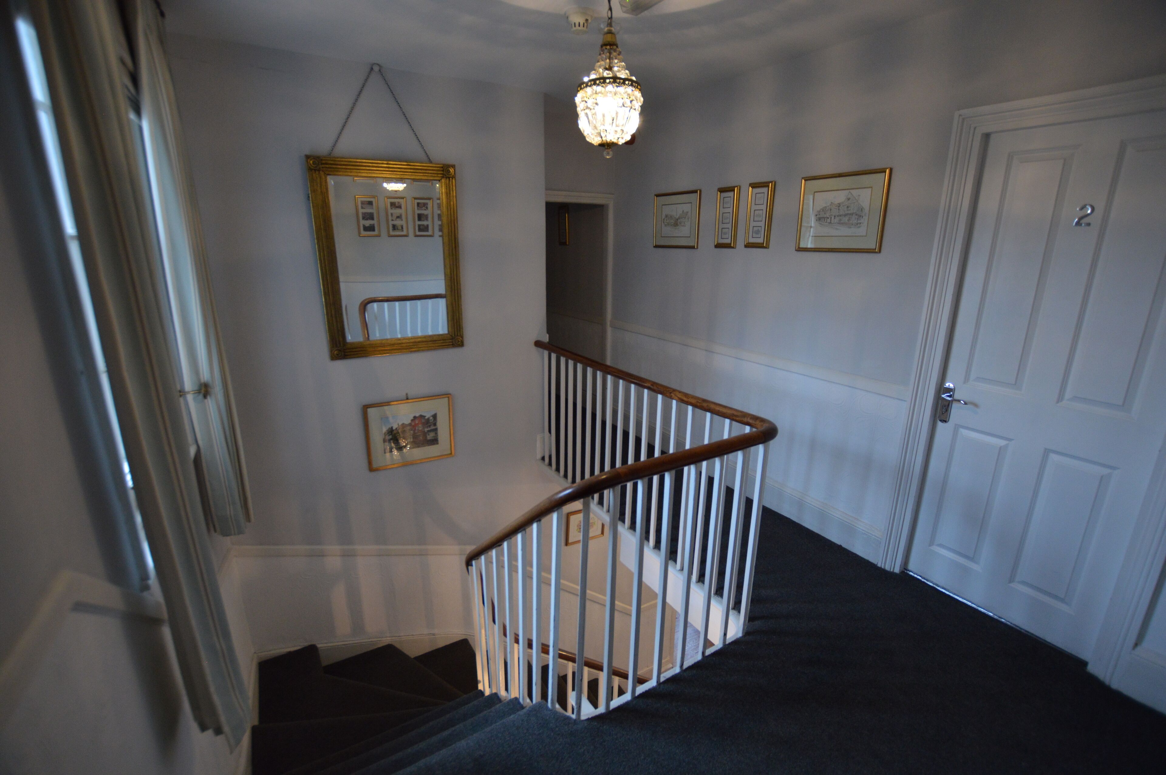 A staircase with a white railing, a chandelier, and framed pictures on the walls.