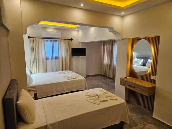 A hotel room with two beds, a TV, a mirror, and a wooden side table. - Sonmez Hotel (Fethiye)