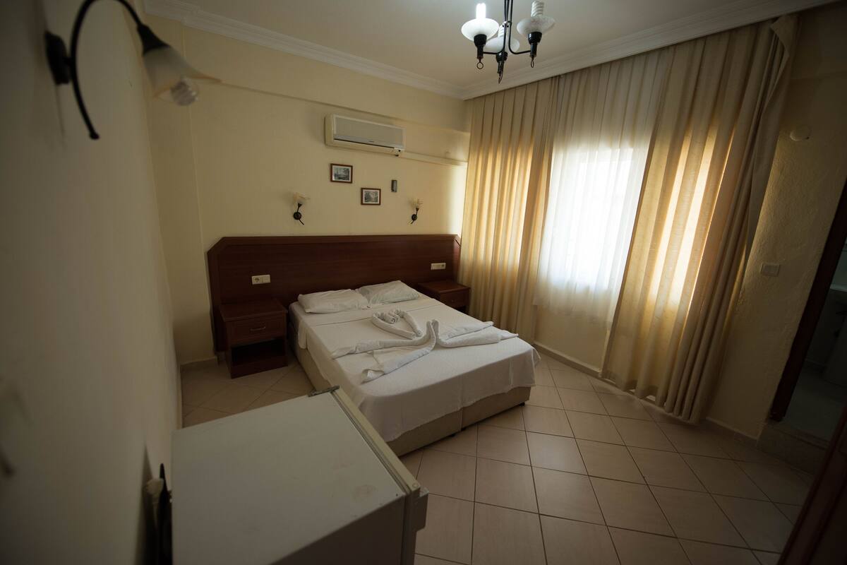 Une chambre d’hôtel avec un lit, une table de chevet, une commode et une fenêtre avec des rideaux.