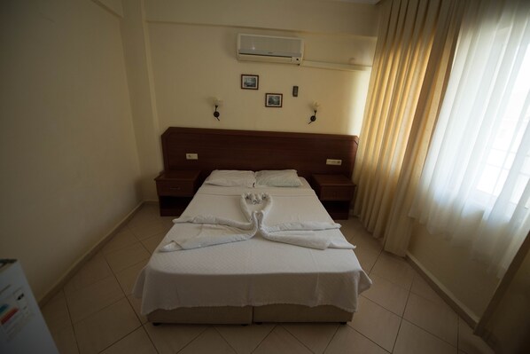 A hotel room with a large bed, two bedside tables, a wall-mounted air conditioner, and a window with curtains. - Sonmez Hotel (Fethiye)