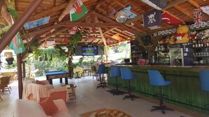 Zona de bar con mesas de billar, taburetes y una pantalla de televisión.