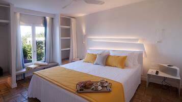 A hotel room with a large bed, a bedside table with a lamp, a tray with breakfast items, and a window with curtains.