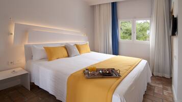 A neatly made bed with a tray of breakfast, a bedside table, and a window with curtains.