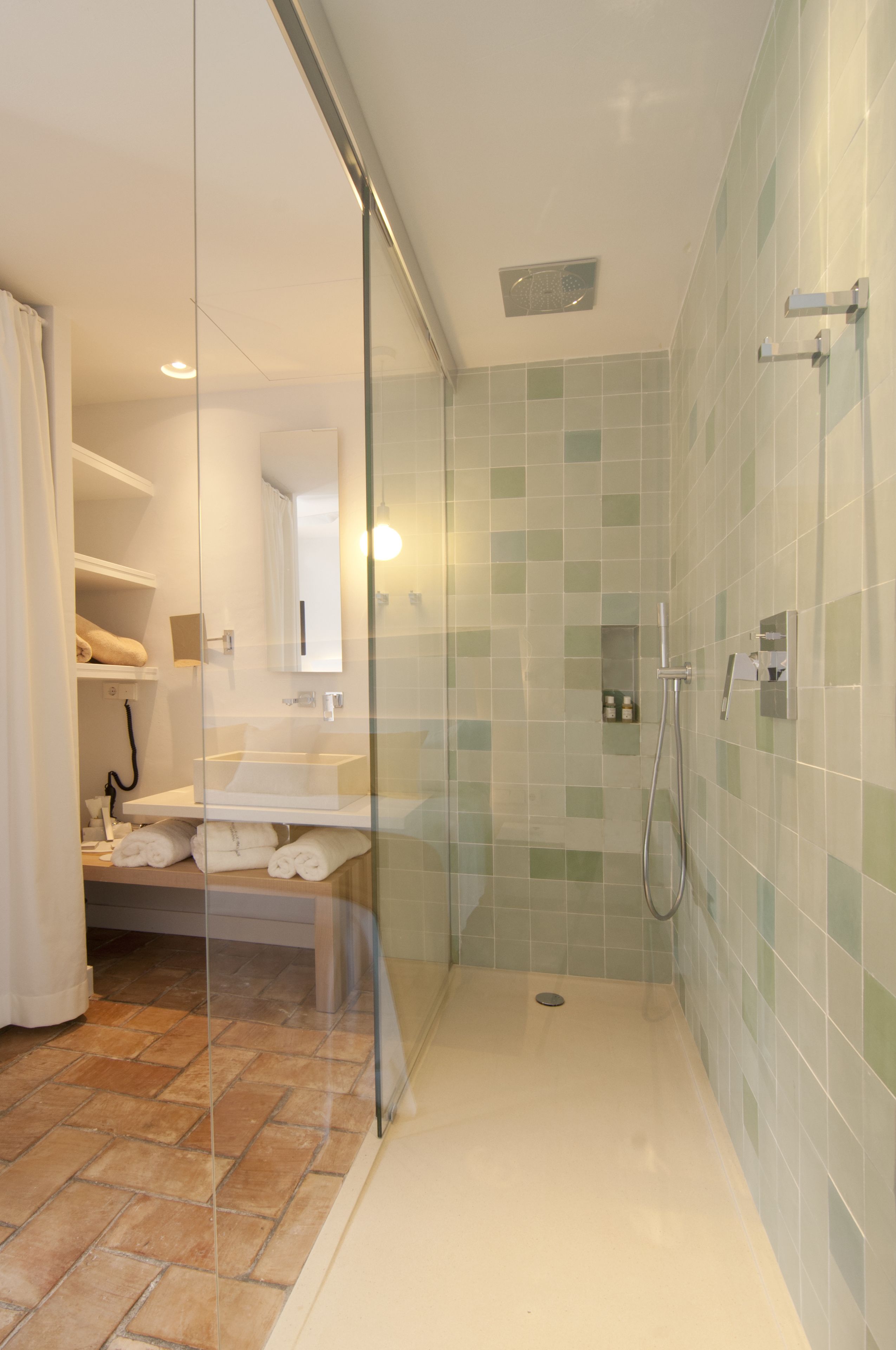 Un baño moderno con cabina de ducha de vidrio, lavamanos blanco y suelo de baldosas.