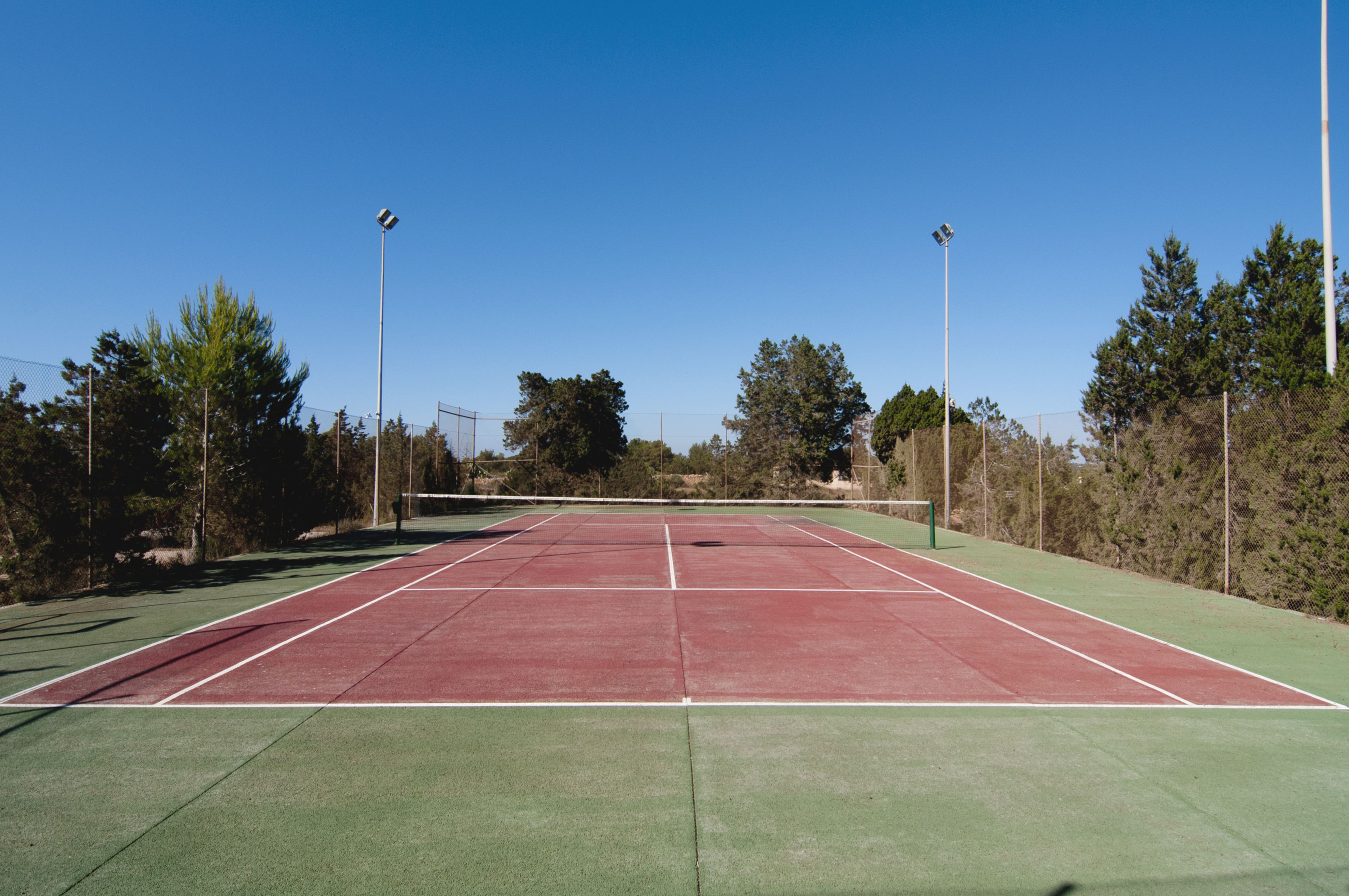 A tennis court with green and red surfaces, surrounded by trees and fencing.