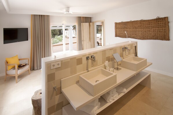 A modern bathroom with a large vanity, dual sinks, and a flat-screen TV mounted on the wall.