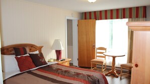 A hotel room with a bed, bedside table, lamp, and a small table with chairs. - Crestwood Inn (Muskoka Lakes)