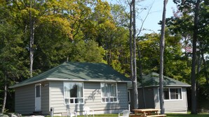 A cabin with a green roof, two white chairs, a picnic table, and a small driveway. - Crestwood Inn (Muskoka Lakes)