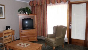 A living room with a television on a wooden cabinet, a chair, a table with a placemat, and a door with a window. - Crestwood Inn (Muskoka Lakes)