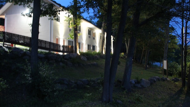 A two-story house with a covered porch, surrounded by trees and a grassy area. - Crestwood Inn (Muskoka Lakes)