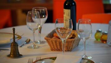 A dining table set with wine glasses, plates, cutlery, and a basket of bread.