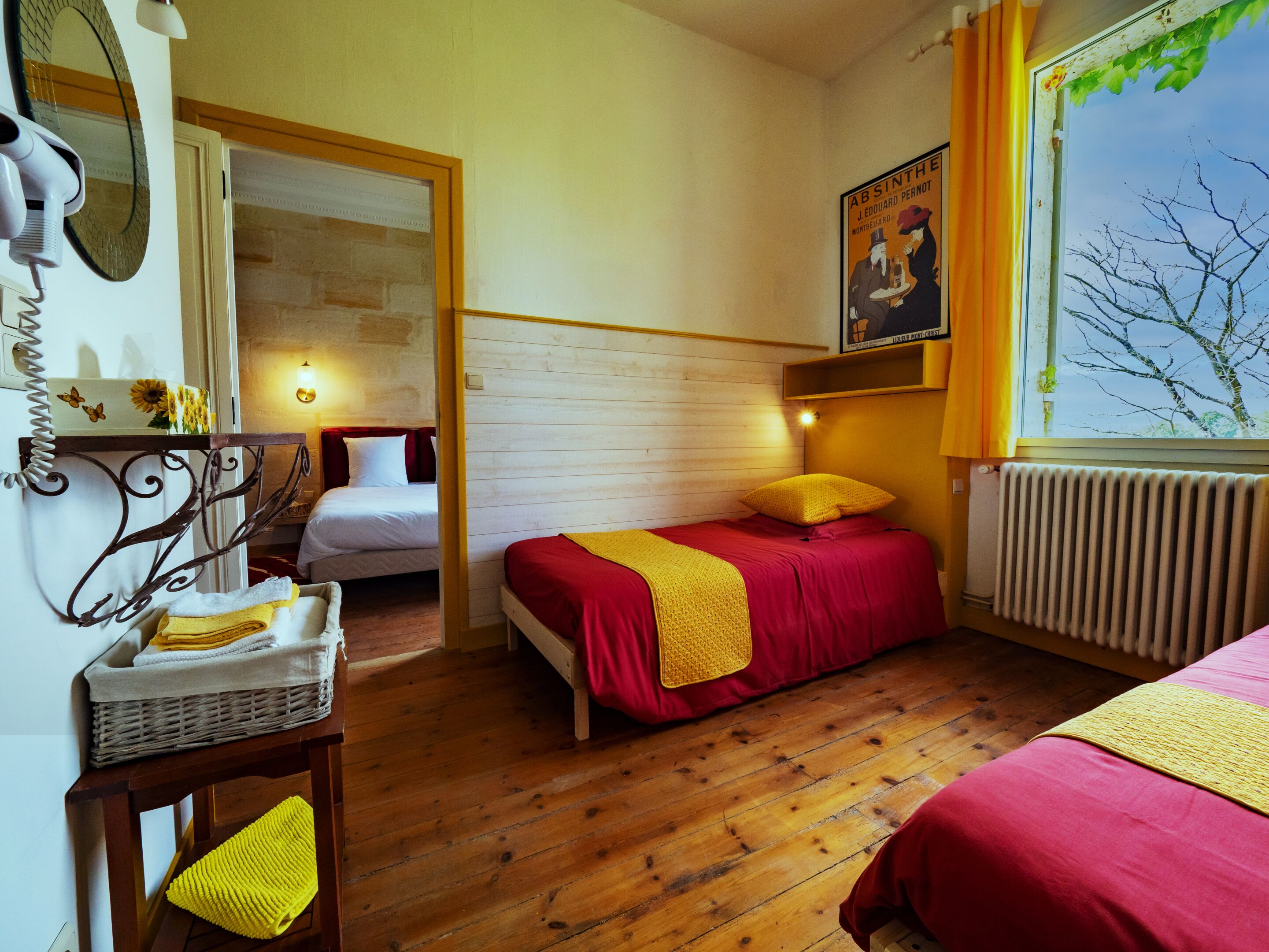 A bedroom with two beds, wooden flooring, a radiator, a mirror, a wall-mounted light, and a poster.