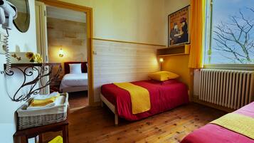 A bedroom with two beds, wooden flooring, a radiator, a mirror, a wall-mounted light, and a poster.