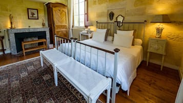 A bedroom with a bed, bench, bedside table, lamp, and fireplace.