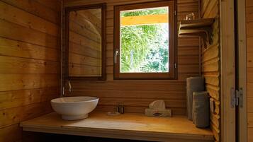 A wooden cabin bathroom with a large window, a sink, and a mirror.