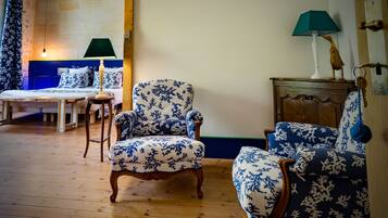 A room with a wooden floor, two blue and white patterned armchairs, a wooden cabinet, a green lamp, and a bed with matching bedding.