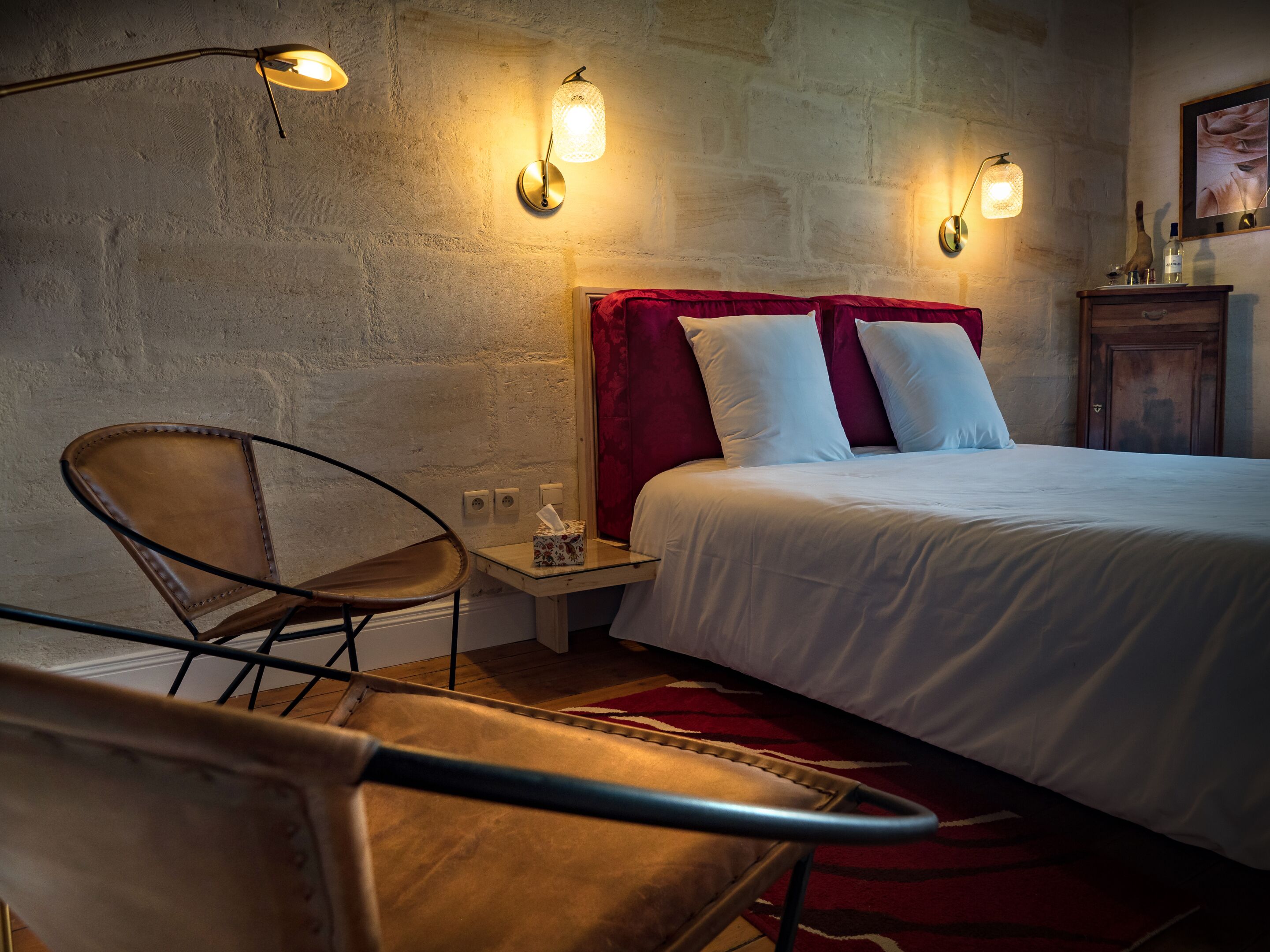 A bedroom with a bed, two wall-mounted lights, a chair, and a nightstand with a tissue box.