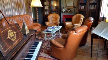 Ein Wohnzimmer mit einem Flügel, Ledersesseln, einem Couchtisch mit Büchern und einem Kamin.