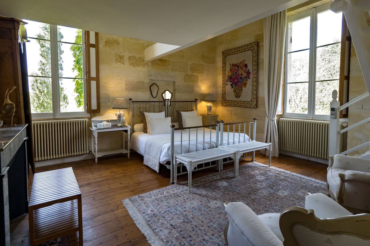 A bedroom with a bed, bedside tables, a nightstand, a window, a radiator, a wooden floor, and a patterned rug.