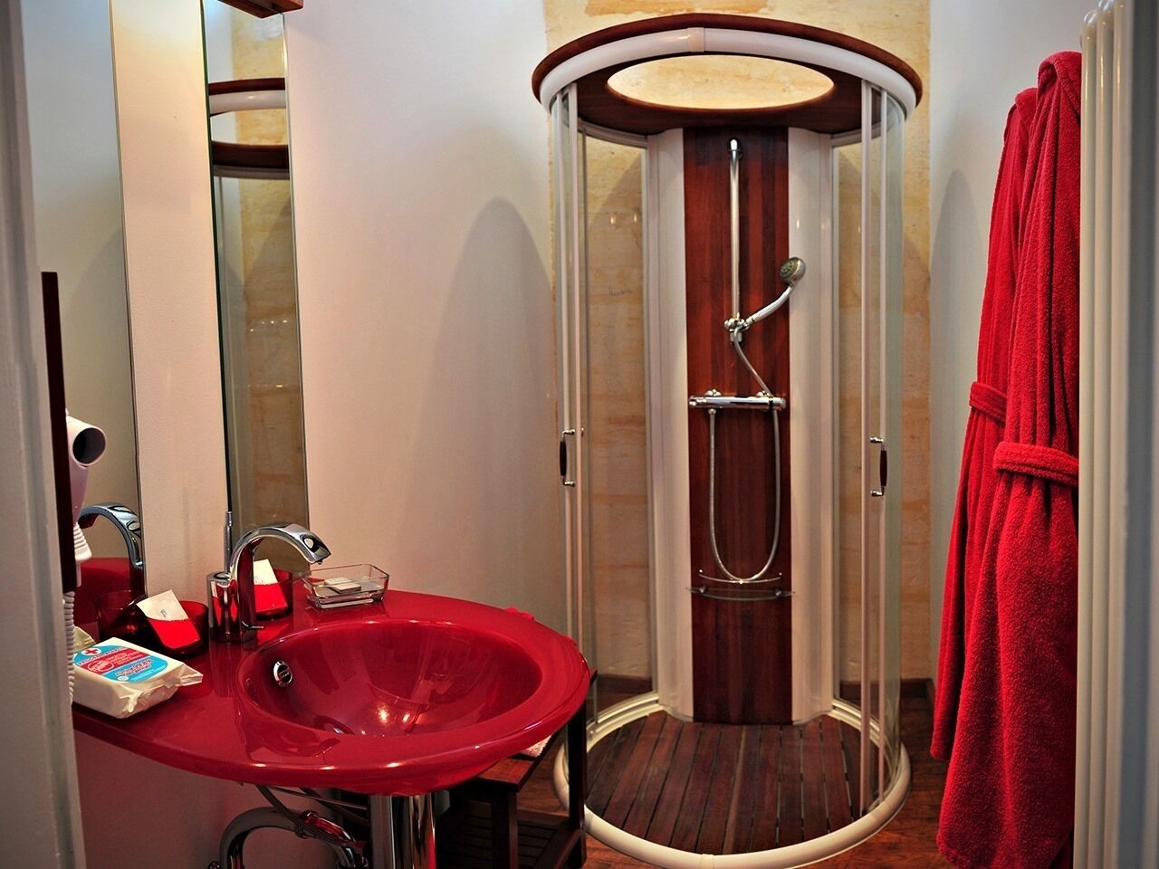 Une salle de bain avec un lavabo rouge, une douche en verre et une serviette rouge accrochée au mur.