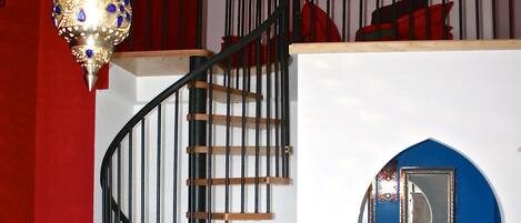 A spiral staircase with a wooden finish and black railings, leading to a blue-walled bathroom with a white sink and mirror.