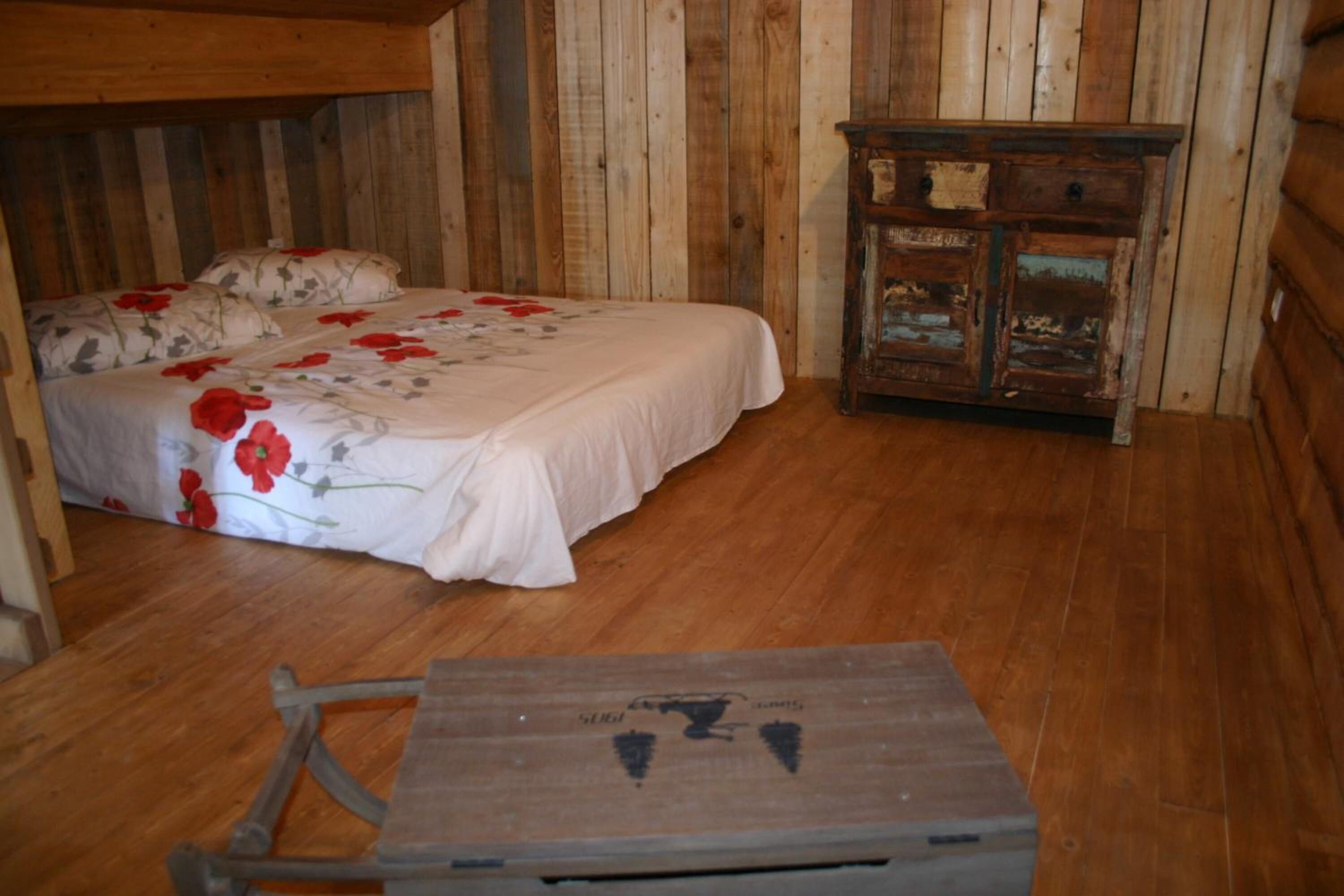 Una habitación tipo cabaña de madera con una cama, un aparador de madera y una mesita.