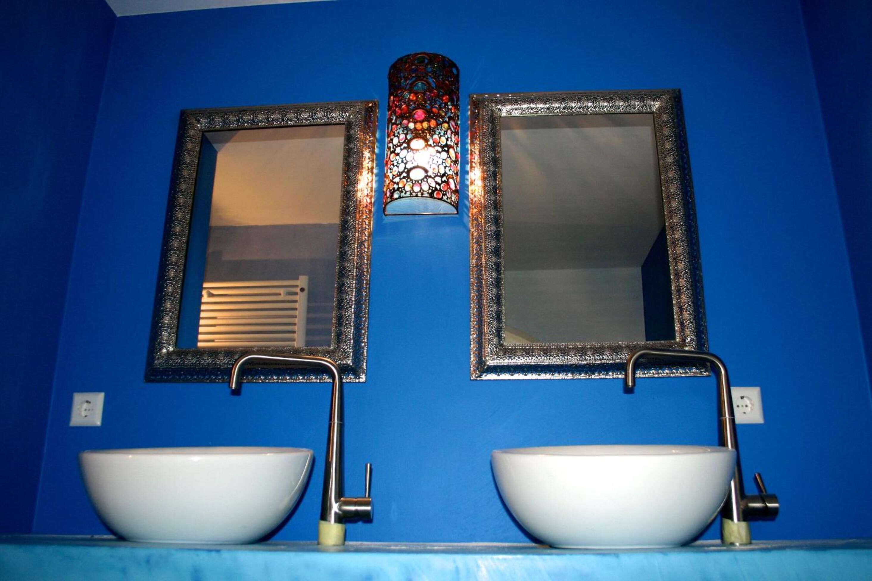 A bathroom with two white sinks, a blue wall, and two mirrors with ornate frames.