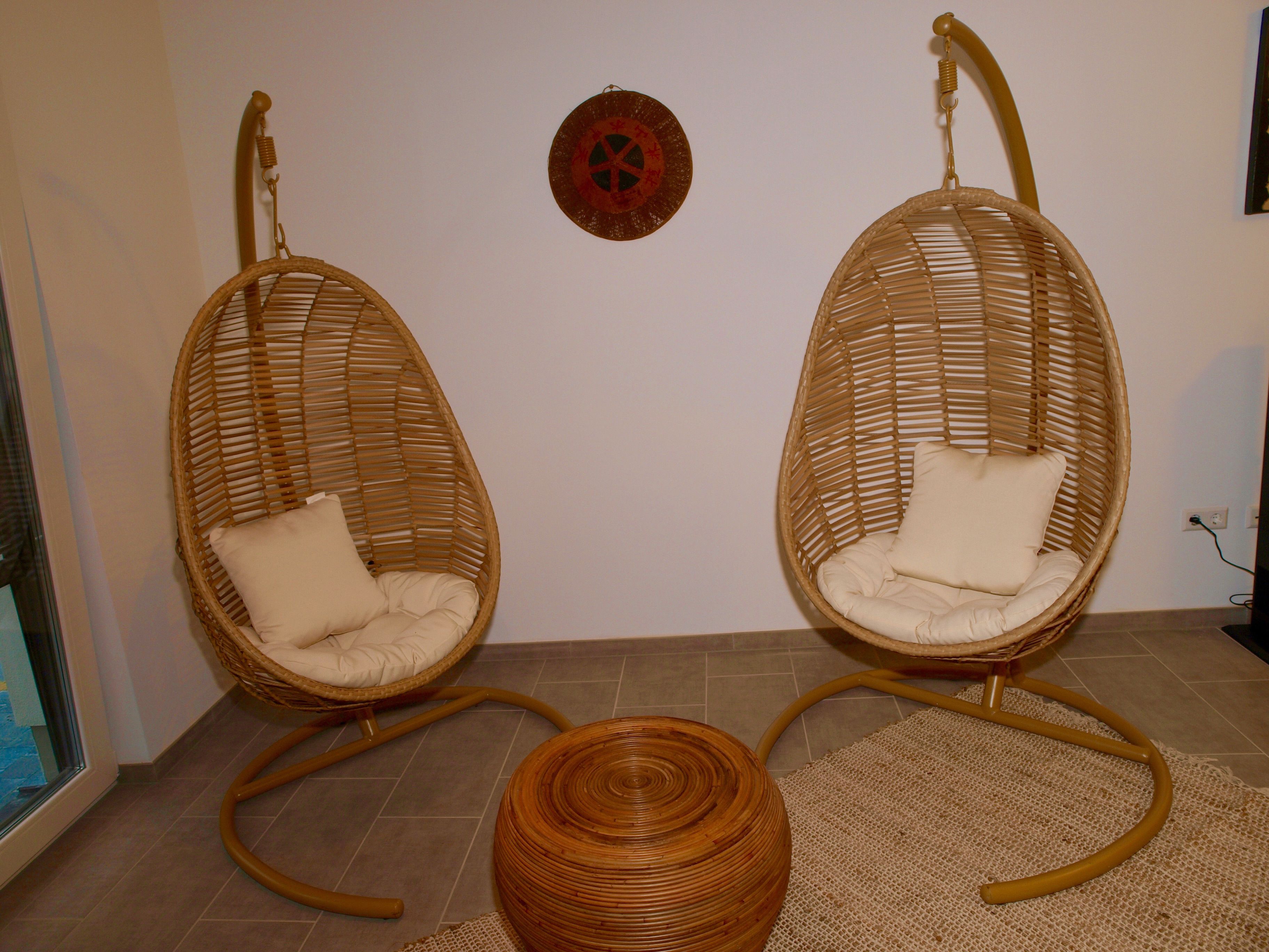 Two wicker chairs with cushions, a woven stool, and a wall-mounted decorative plate.