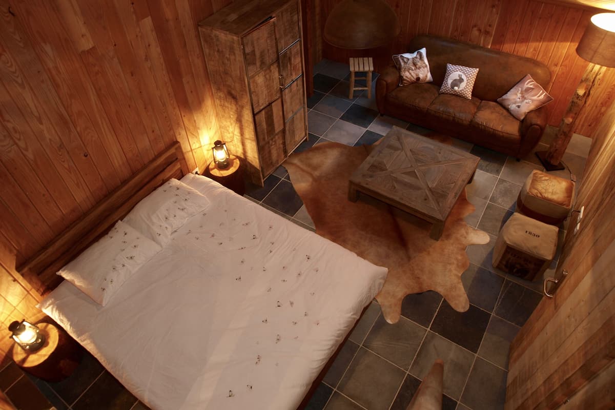 Une pièce confortable avec un lit, une armoire en bois, un canapé agrémenté de coussins à motifs et un petit tabouret.