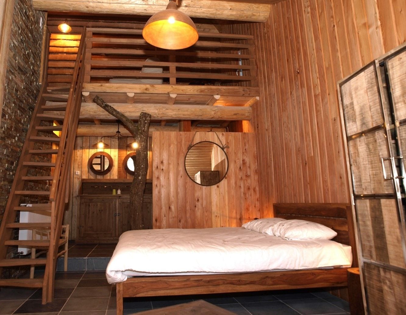 Une chambre à coucher de style cabane en bois, avec un lit, une échelle et un miroir rond accroché au mur.
