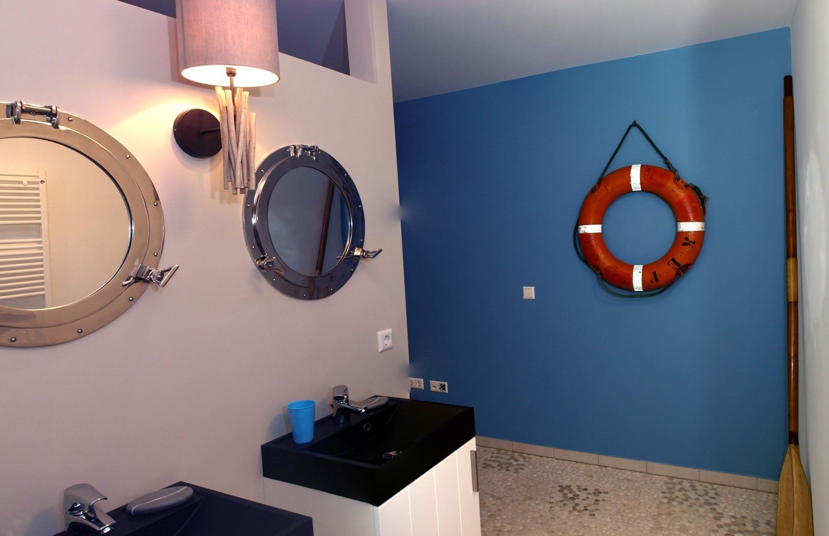 A bathroom with two round mirrors, a sink, and a life preserver hanging on the wall.