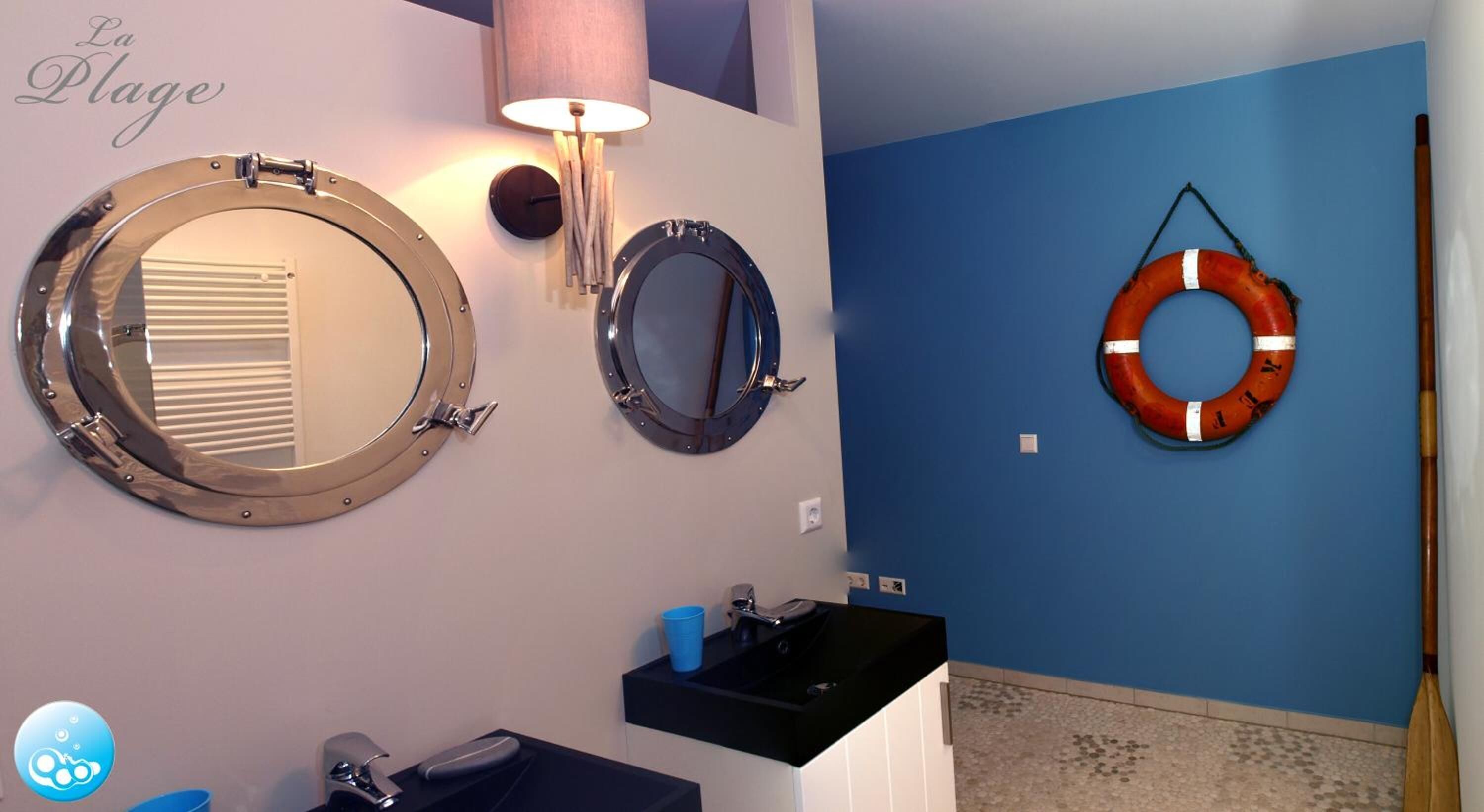 A bathroom with two round mirrors, a blue wall, a life ring, and a mop.