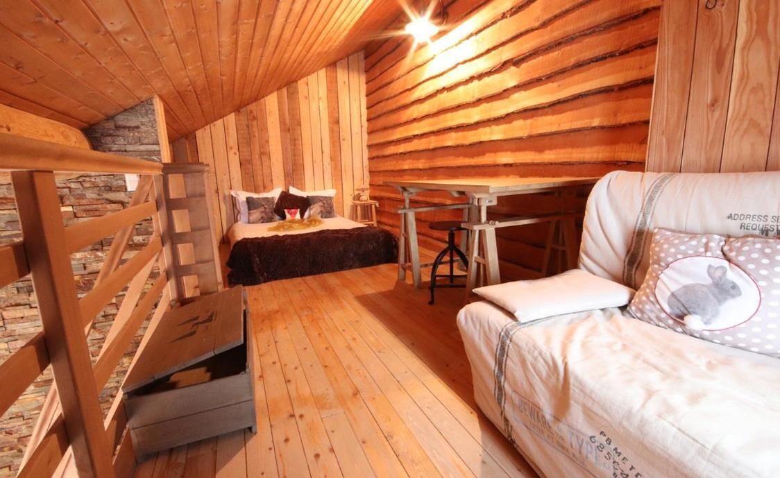 A cozy cabin with a wooden interior, a bed with a dark blanket, a small table, and a sofa with a pillow featuring a rabbit.