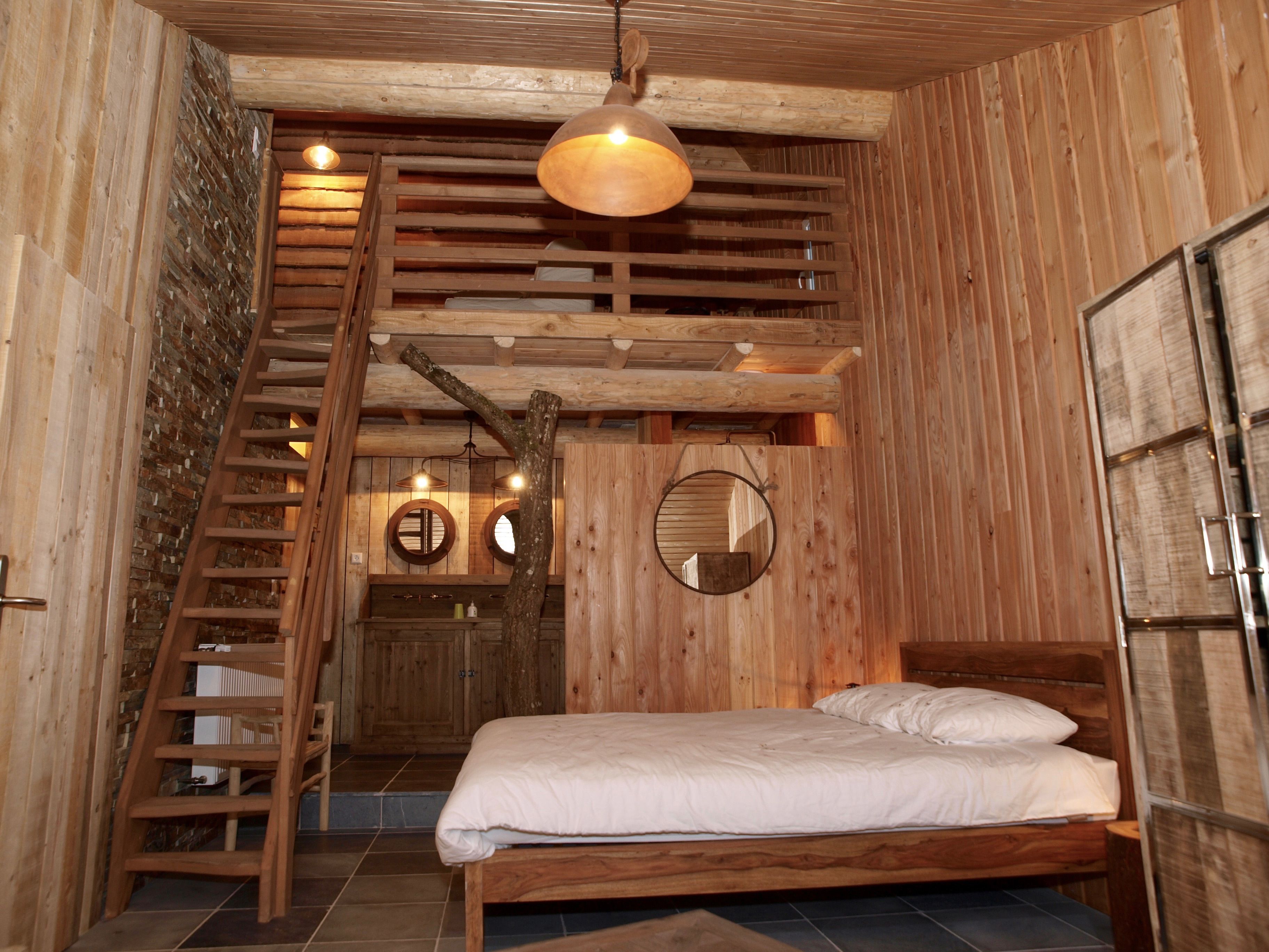 L’intérieur d’une cabane en bois, avec un lit, une échelle en bois et un miroir rond accroché au mur.