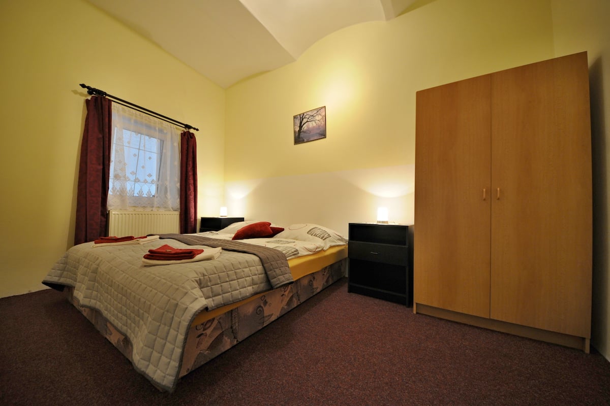 A bedroom with a bed, a wardrobe, a nightstand, a window with curtains, and a wall-mounted picture.