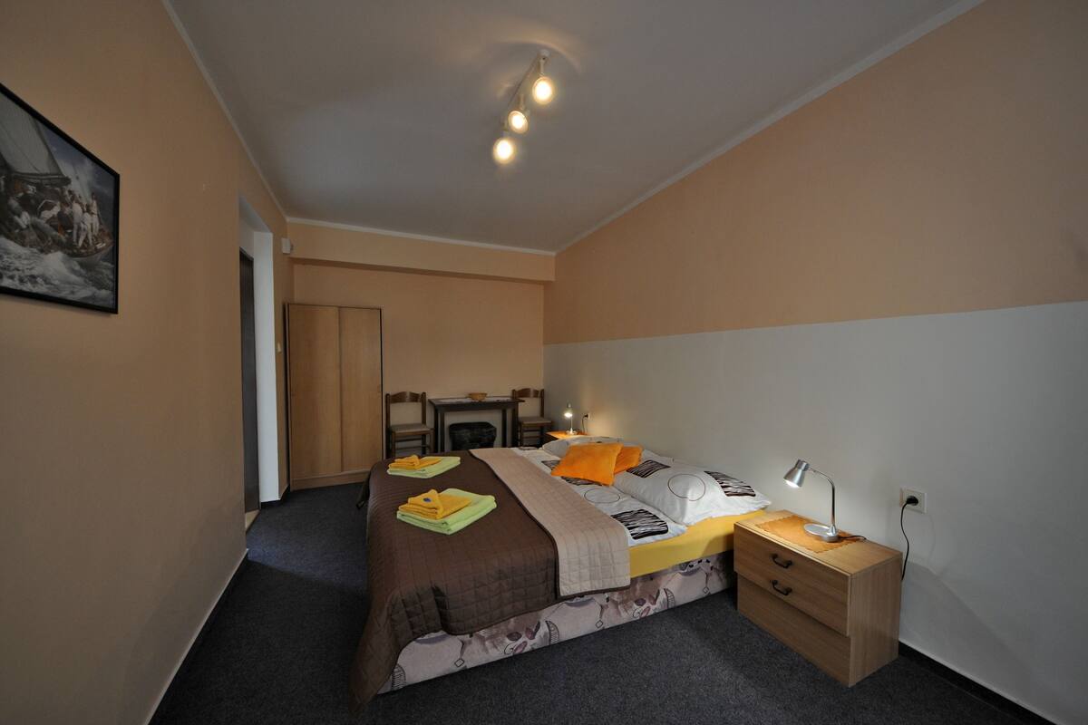 A bedroom with a bed, bedside table, lamp, and a desk with chairs.