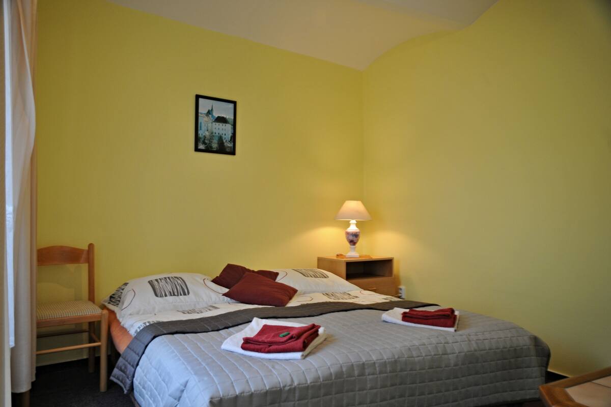 A hotel room with a bed, a chair, a nightstand with a lamp, and a picture on the wall.