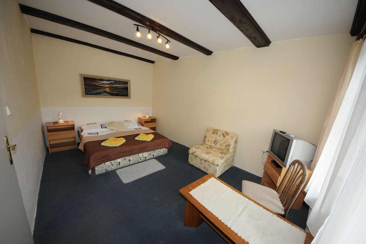A bedroom with a bed, a chair, a desk, a television, and a painting on the wall.