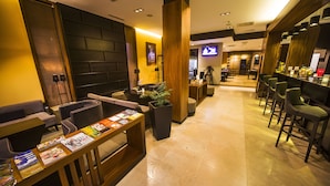 Um hall de hotel moderno com área de bar, assentos e uma tela de televisão.