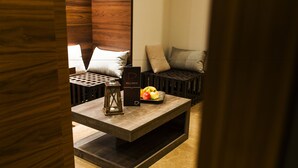 Uma área de estar moderna com um banco de madeira escura, uma mesinha com uma cesta de frutas e uma placa com a palavra 'Wellness'.