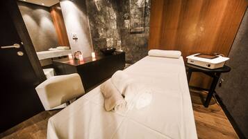 A modern spa room with a massage table, a wooden cabinet, a sink, and a small table with a device.