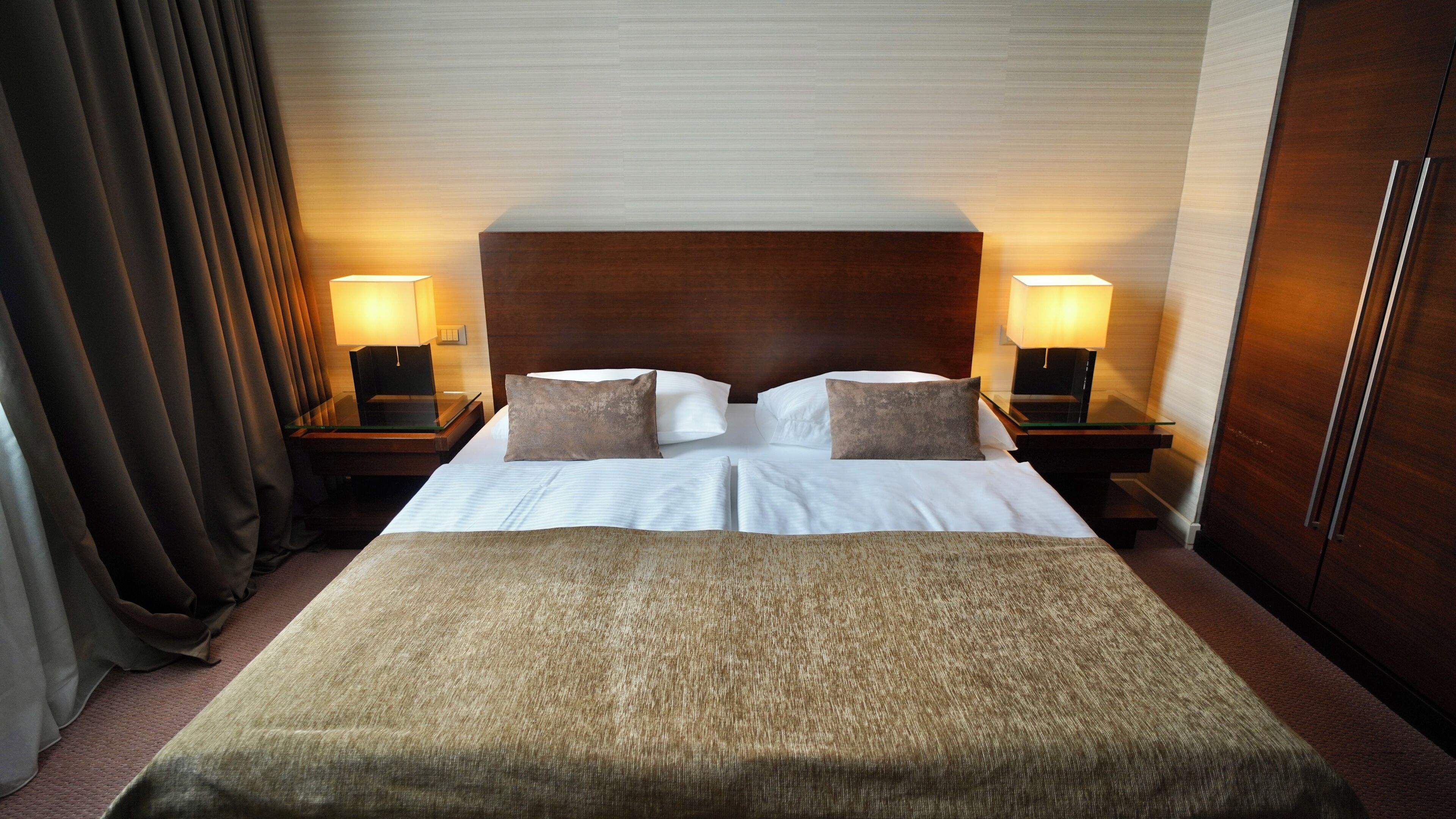 Une chambre d’hôtel avec un grand lit, deux tables de chevet avec des lampes, une tête de lit en bois et une grande fenêtre avec des rideaux.