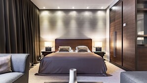 Quarto de hotel moderno com uma cama grande, cortinas escuras, um vaso sobre uma mesa e um guarda-roupa.